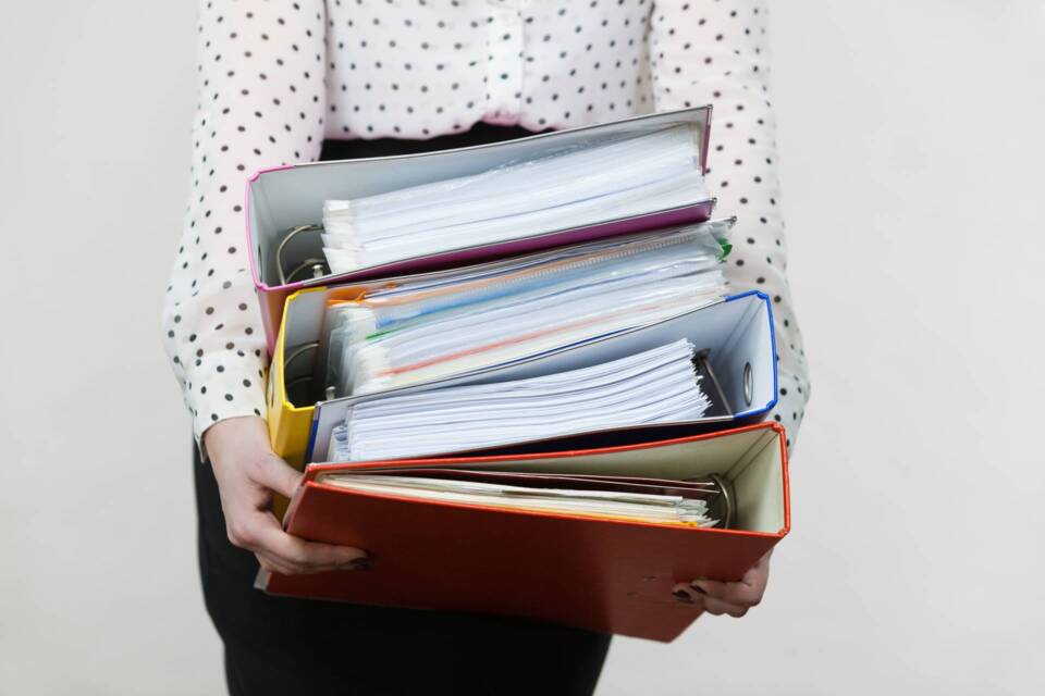 Woman holding heavy colorful binders with documents