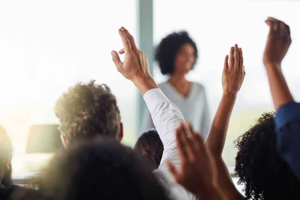 People raising hands to ask questions of a presenter.