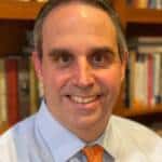 Warm smiling man in professional attire with bookshelves in the background - Darby Integrative Counseling.